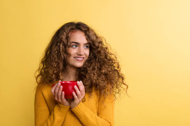 портрет молодой женщины с красной чашкой в студии на желтом фоне. - curley cup стоковые фото и изображения