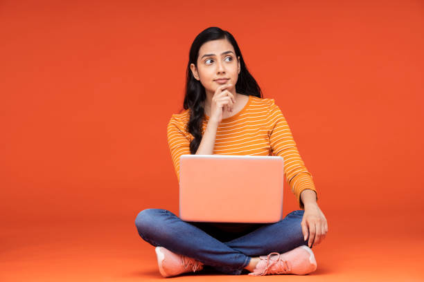 portrait of a young women sitting isolated over orange background stock photo