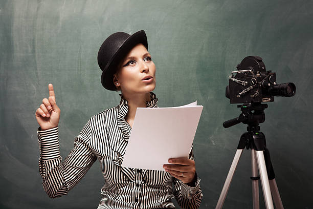 Portrait of actress reading script behind camera Portrait of actress reading script behind camera.The camera is on the right side of frame and young woman is on the left side.She is wearing a striped shirt and a bowler hat and holding the paper she reads.Shot with a full frame DSLR camera.  actress stock pictures, royalty-free photos & images