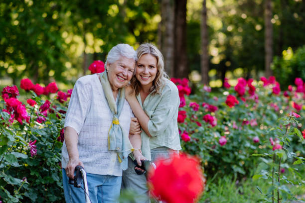 Portrait of adult granddaughter with senior grandmother on walk in park, with roses at background stock photo