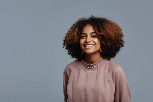 Minimal portrait of young African-American woman with natural curly hair smiling at camera against blue background, copy space
