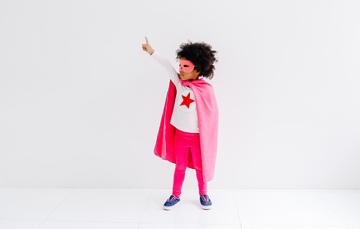Portrait of African American little child girl plays superhero on the white wall background. Girl power concept. Happy Time.