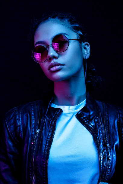 portrait of an African American young woman in sunglasses isolated on a black background in neon light stock photo