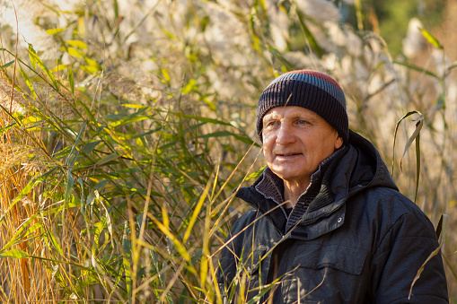 Portrait of an elderly man in the tall grass on the lake shore. The concept of travel in the autumn season