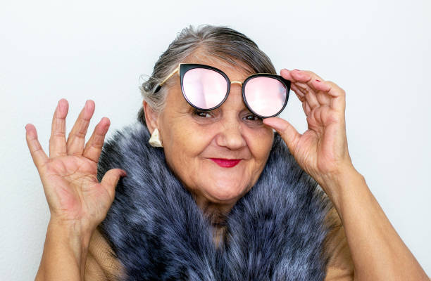 Portrait of an elderly woman with glasses. An old hipster lady with a fur collar and sunglasses. Older people, the concept of fashion. A fashionable hipster woman poses for the camera stock photo