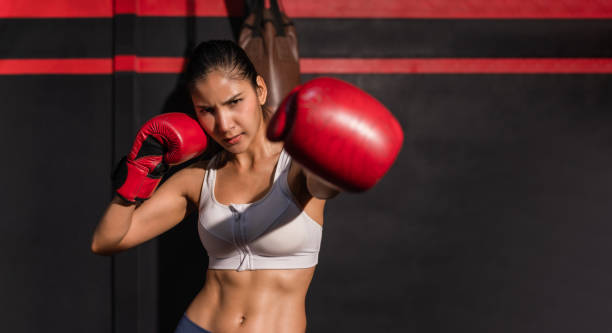 Portrait of asian attractive woman in sportswear wear red boxing gloves with workout and pose boxing show punch in gym. stock photo
