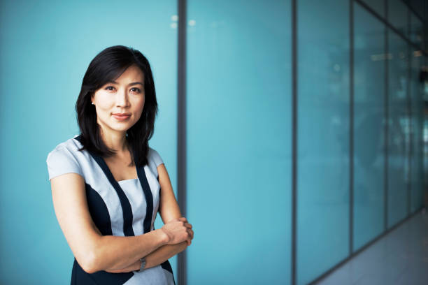 Portrait of asian business woman in corporate office Business woman standing looking into camera woth folded hands smiking in a corporate office asian middle-aged woman formal stock pictures, royalty-free photos & images