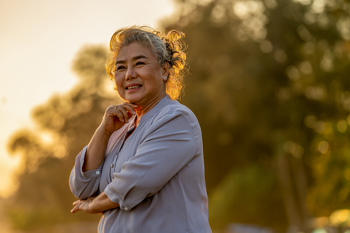 Portrait of Happy beautiful Asian senior woman walking on tropical beach at summer sunset. Healthy retirement elderly female relax and enjoy outdoor lifestyle activity in summer travel vacation