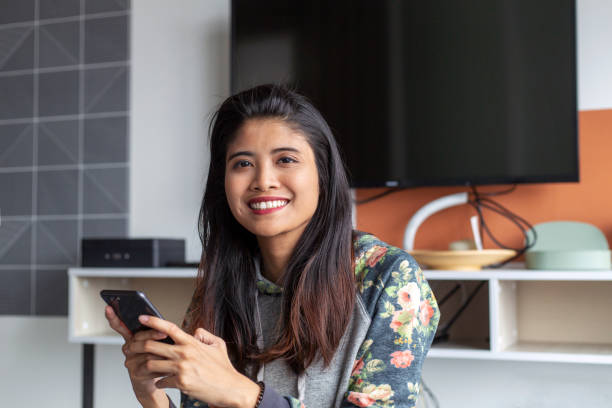 portrait of asian woman looking at camera portrait of southeaast asian woman stay at home, holding a phone, relaxing and looking into camera indonesian woman stock pictures, royalty-free photos & images
