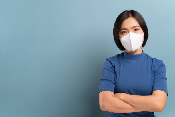 파란색 배경에 고립 된 위생 마스크를 착용한 아시아 여성의 초상화 - n95 mask 뉴스 사진 이미지