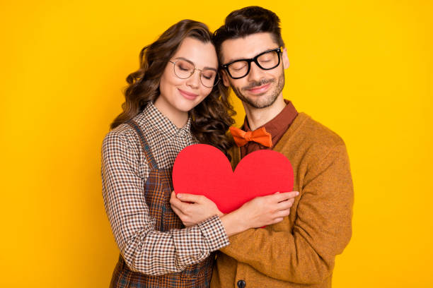 Portrait of attractive cheerful amorous couple friends friendship embracing heart shape isolated on bright yellow color background stock photo