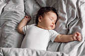 istock Portrait of baby in sleepwear lying under gray blanket on bed at home. Sleeping on back infant child in bedroom, see sweet dream. Grey background, free copy space. Childcare and healthy sleep concept 1383504420