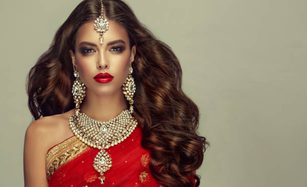Portrait of beautiful girl dressed in a traditional indian national suit and posh "kundan style" jewelry set. Young attractive woman, covered by traditional indian red shawl (dupatta) and dressed in hand-made "kundan style" jewelry set. Posh jewelry set is consisting of big earrings, bright necklace and head adornment (tikka). Perfect, dense, wavy, freely flying hair and "smoky eyes" style makeup. indian jewelry stock pictures, royalty-free photos & images