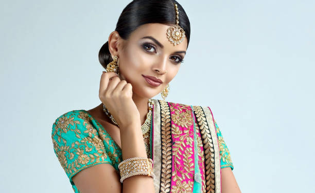 Portrait of beautiful girl dressed in a traditional indian national suit, jewelry set, blouse and shawl (dupatta). Young attractive woman, dressed in a traditional indian suit-sari, with green blouse and shawl (dupatta) with gilded hand-made decoration. Posh jewelry set is consisting of big earrings, bright necklace, head adornment (tikka) and gold nose ring. indian jewelry stock pictures, royalty-free photos & images