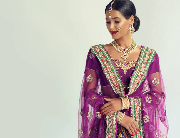 Portrait of beautiful girl dressed in a traditional indian national suit, jewelry set, blouse and shawl (dupatta). Young attractive woman, dressed in a traditional indian suit-sari, with purple blouse and shawl (dupatta) with gilded hand-made decoration. Posh jewelry set is consisting of big earrings, bright necklace, head adornment (tikka) and gold nose ring. indian jewelry stock pictures, royalty-free photos & images