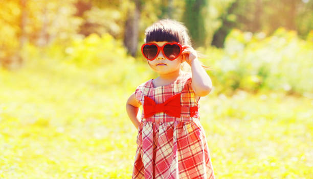 Portrait of beautiful little girl child wearing red heart shaped sunglasses outdoors in sunny summer park stock photo