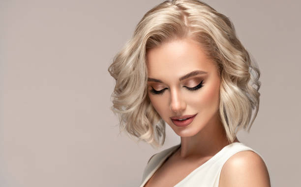 Portrait of beautiful looking young blonde woman with the middle length hair performed in elegant hairstyle.Elegance and hairstyling. Portrait of beautiful looking young blonde woman with the middle length hair performed in elegant hairstyle. Lady wearing in a delicate makeup.Perfect model is shyly looking down. Beauty, elegance, hairstyling and cosmetics. white hair young woman stock pictures, royalty-free photos & images