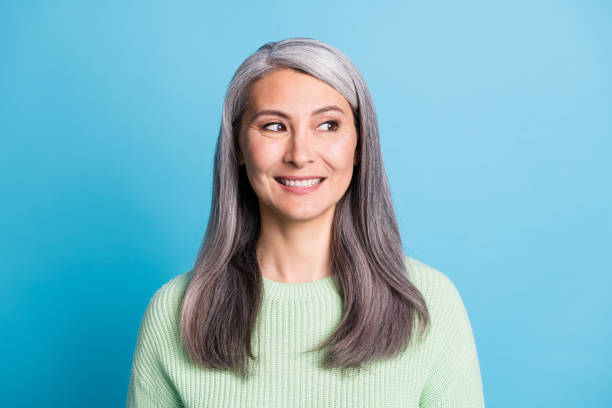 retrato de hermosa mujer madura sonriente vestida jersey verde aislado en fondo de color azul - cabello gris fotografías e imágenes de stock