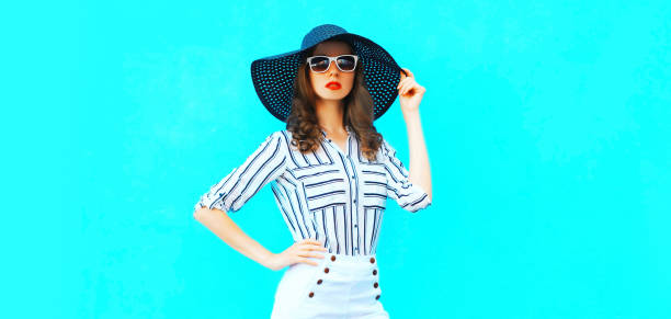 Portrait of beautiful woman model wearing black round summer hat, white striped shirt on blue background stock photo
