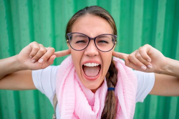 Portrait of Beautiful Woman Screaming with Fingers in Ears against Green Background - stock photo Portrait of Beautiful Woman Screaming with Fingers in Ears against Green Background Fingers in Ears stock pictures, royalty-free photos & images