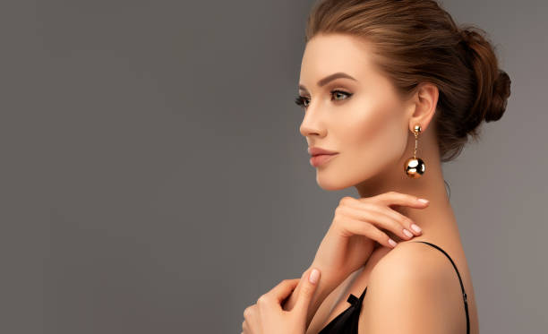 Portrait of beautiful woman with a misty look. Makeup and cosmetic. Portrait of perfectly looking woman dressed in splendid evening makeup. Ripe lips, painted in rose color, long black eyelashes and gilded eyelids. Big golden balls of earrings in her ears. Mystic and misty look in her eyes. female likeness stock pictures, royalty-free photos & images