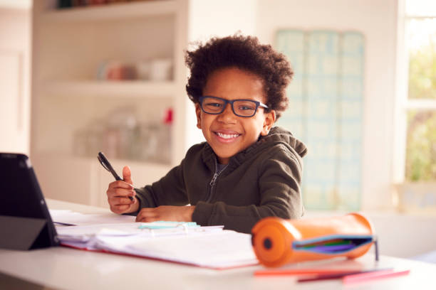 Portrait Of Boy Sitting At Kitchen Counter Doing Homework Using Digital Tablet Portrait Of Boy Sitting At Kitchen Counter Doing Homework Using Digital Tablet boys glasses stock pictures, royalty-free photos & images