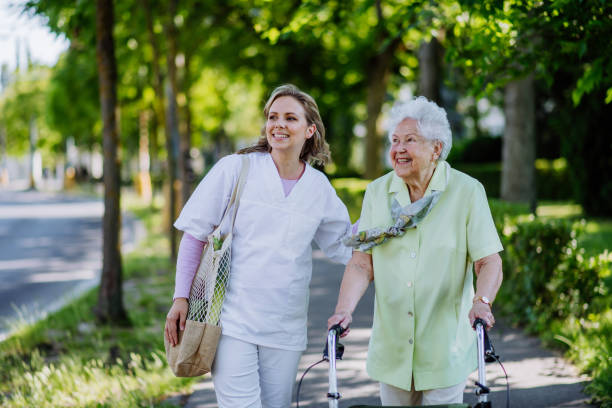 Portrait of caregiver with senior woman on walk in park with shopping bag, looking at caemra. stock photo