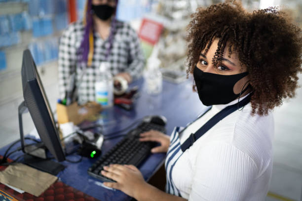 portrait of cashier wearing face mask working in a store - balcão computador imagens e fotografias de stock