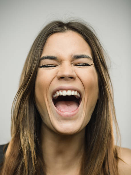 Portrait of caucasian young woman with very excited expression and eyes closed Close up portrait of caucasian young woman with excited expression shouting or singing with eyes closed against white gray background. Vertical shot of spanish real people excited in studio with long brown hair. Photography from a DSLR camera. Sharp focus on eyes. mouth open stock pictures, royalty-free photos & images