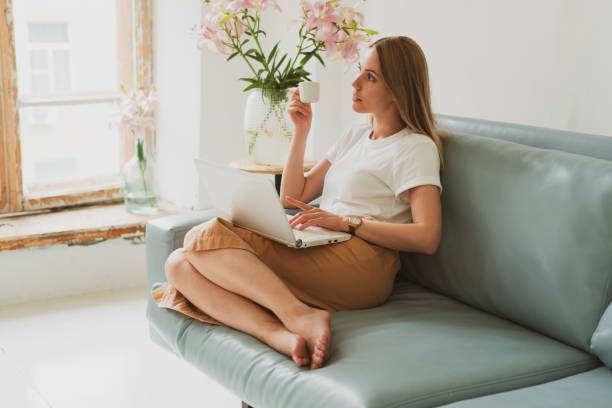 portrait of charming young woman with laptop working at home while sitting on sofa stock photo