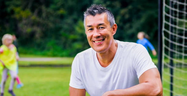 portrait of coach crouching on soccer field - coach stockfoto's en -beelden