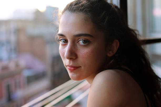 Portrait of confidence girl with freckles at the window at sunset, during lockdown stock photo