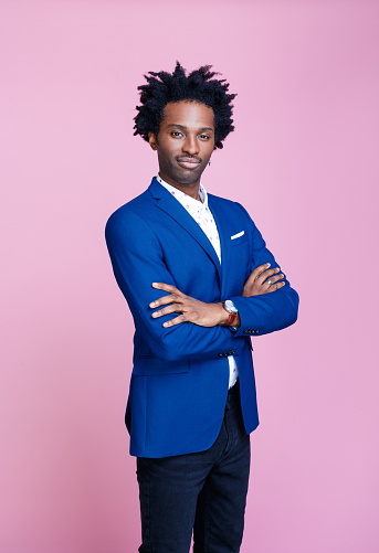 Cheerful afro american man wearing navy blue suit jacket and white shirt, standing with arms crossed and looking at camera. Studio shot on pink background. Portrait of designer.