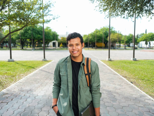Portrait of confident latin male student A horizontal portrait of a latin male student looking at camera outdoors with college campus background. medium shot stock pictures, royalty-free photos & images