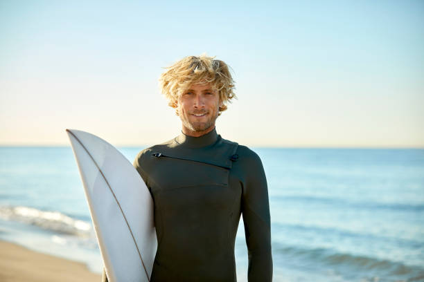 porträt von zuversichtlich mann mit surfbrett am strand - surfer stock-fotos und bilder