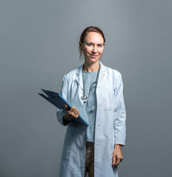 Portrait of confident mature doctor against wall stock photo