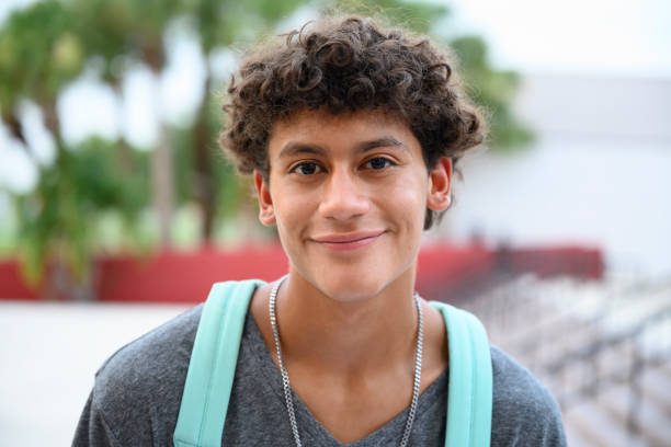 Portrait of contented male Hispanic teenager Headshot of smiling Hispanic teenage boy standing outside school with backpack and looking at camera before going to class. 16 17 years stock pictures, royalty-free photos & images