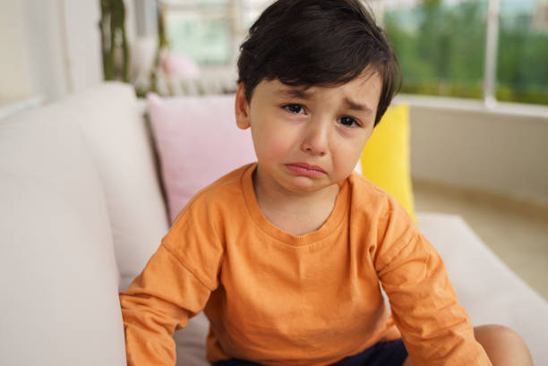 Portrait of crying innocent toddler boy sitting on a sofa at the balcony stock photo