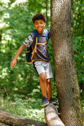 Portrait of cute African boy balancing on the log in the woods.