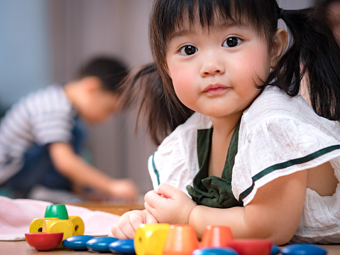 Portrait of cute Asian preschool age girl lie on the floor looking at camera in Montessori classroom