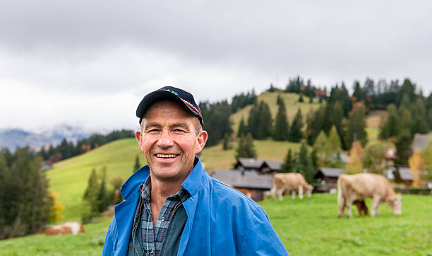Portrait Of Dairy Farmer In Field With Cattle Portrait Of Farmer, with hat In meadow With his cows in Switserland rancher stock pictures, royalty-free photos & images