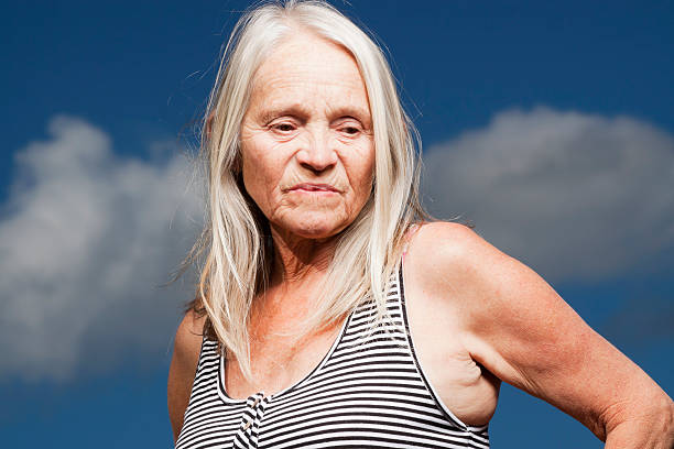 Portrait of disgusted mature blond woman against dramatic background Portrait of disgusted mature woman with blonde straight long hair agains dark sky, full frame horizontal composition with copy space ugly old women stock pictures, royalty-free photos & images