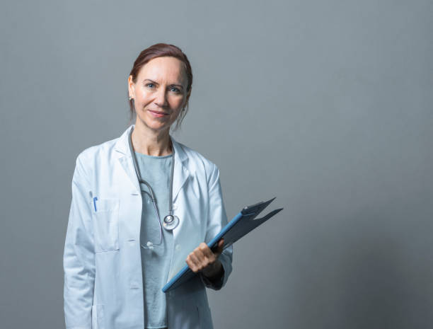 portrait of doctor with clipboard against wall - doctor wall imagens e fotografias de stock