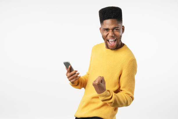 Portrait of excited young man with mobile phone isolated over white background and celebrating Background, African Ethnicity, People, Males, Copy Space ecstatic stock pictures, royalty-free photos & images