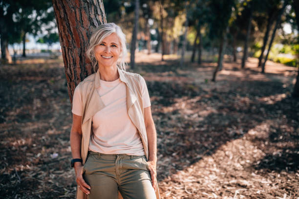 Portrait of fashionable senior woman with gray hair in nature Portrait of beautiful smiling fashionable mature woman standing under tree in forest park in summer mature women beauty beautiful fashion model stock pictures, royalty-free photos & images