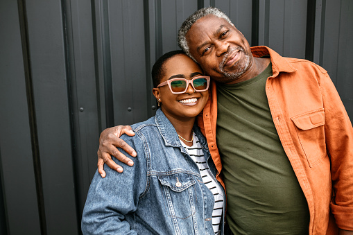 Senior father and daughter posing for photo. Standing in a front of a black door background, embracing, smiling, looking at camera.