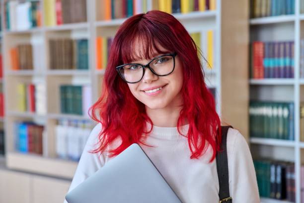 Portrait of female college student in glasses with laptop backpack, looking at camera stock photo