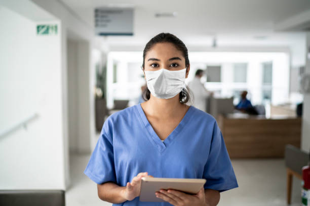 porträt der krankenschwester, die digitale tablette im krankenhaus mit schutzmaske hält - pflege stock-fotos und bilder