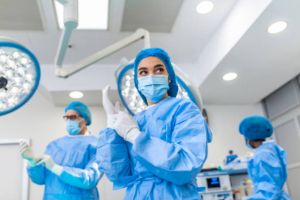 Portrait of female surgeon in surgical uniform in operation theater looking away. Doctor in scrubs and medical mask in modern hospital operating room. stock photo