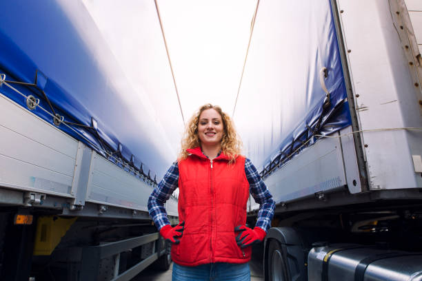 Portrait of female trucker proudly standing between trailers and truck vehicle. Transportation service. Truck driver standing by the truck. truck driver stock pictures, royalty-free photos & images